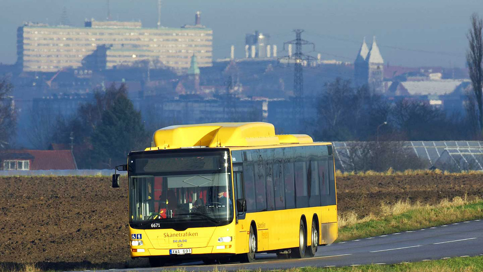 Gul regionbuss i landskap med universitetssjukhuset Lund i bakgrunden.