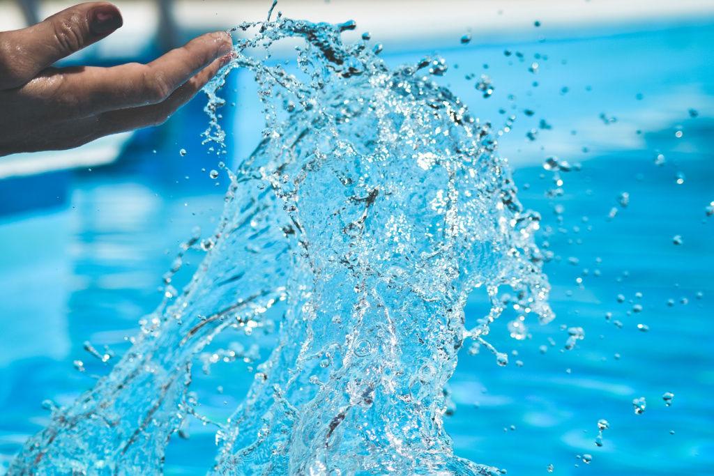 En hand skvätter upp vatten från en pool.