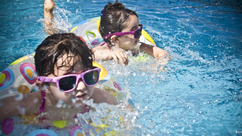 Två flickor med solglasögon och badringar badar i pool.